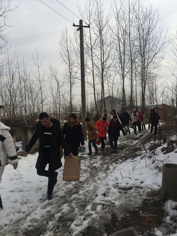 商會愛心慰問團團友正帶著尉問物品，踏著泥雪，迎著寒風，步入村道、前往慰問家庭